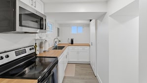 Une cuisine moderne avec des meubles blancs, un four à micro-ondes encastré, une cuisinière et une machine à café.