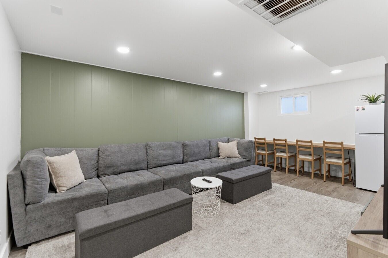 A modern living room with a grey sectional sofa, a small round coffee table, and a dining area with wooden chairs and a white table.