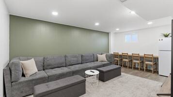 A modern living room with a grey sectional sofa, a small round coffee table, and a dining area with wooden chairs and a white table.