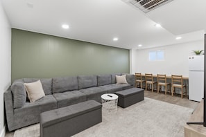 Una sala moderna con un sofá seccional gris, una pequeña mesa redonda y un comedor con sillas de madera y una mesa blanca.