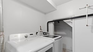 Un espace buanderie comprenant un lave-linge et un sèche-linge Samsung, une conduite métallique et un mur blanc.