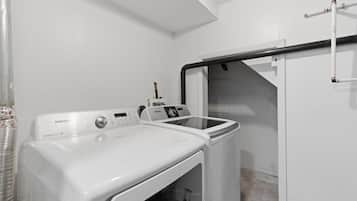 A laundry area with a Samsung washing machine and dryer, a metal pipe, and a white wall.