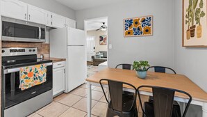 Une cuisine avec des meubles blancs, un four à micro-ondes, une cuisinière et un coin repas comprenant une table et des chaises.