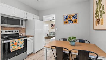 A kitchen with white cabinets, a microwave, a stove, and a dining area with a table and chairs.