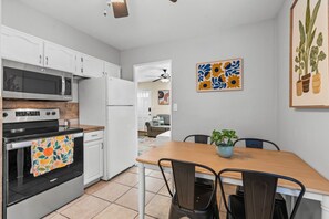 A kitchen with white cabinets, a microwave, a stove, and a dining area with a table and chairs. - 1950s Bungalow in Millcreek | Spacious & Central (South Salt Lake)