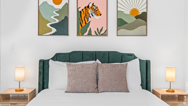 Une chambre à coucher avec un lit, deux tables de chevet et trois œuvres d’art encadrées accrochées au mur.