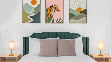 A bedroom with a bed, two bedside tables, and three framed artworks on the wall.