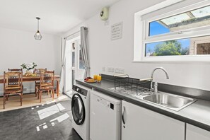 A compact kitchen with a washing machine, a sink, and a dining area with a table and chairs. - Modern 3BR Home Perfect for Groups and families (Little Hulton)