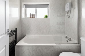 A bathroom with a bathtub, a window, a towel rack, and a shower head. - Modern 3BR Home Perfect for Groups and families (Little Hulton)