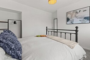 Ein Schlafzimmer mit einem Bett, einem Nachttisch, einer Lampe, einem Wandbild und einer Tür.