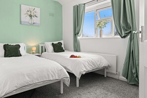 A bedroom with two beds, a window with curtains, a radiator, and a bedside lamp. - Modern 3BR Home Perfect for Groups and families (Little Hulton)