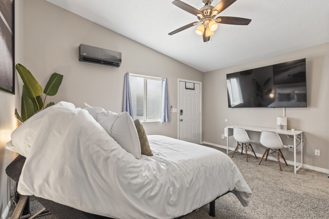 A bedroom with a bed, a desk, a chair, a television, and a ceiling fan.