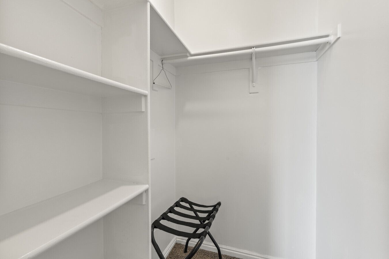 A walk-in closet with white walls, a black metal chair, and open shelving units.