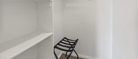 Un vestidor con paredes blancas, una silla de metal negro y estanterías abiertas.