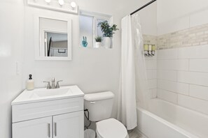 A bathroom with a white sink, mirror, toilet, and shower area. - Cozy Millcreek Studio w/ Laundry & Comfort (South Salt Lake)