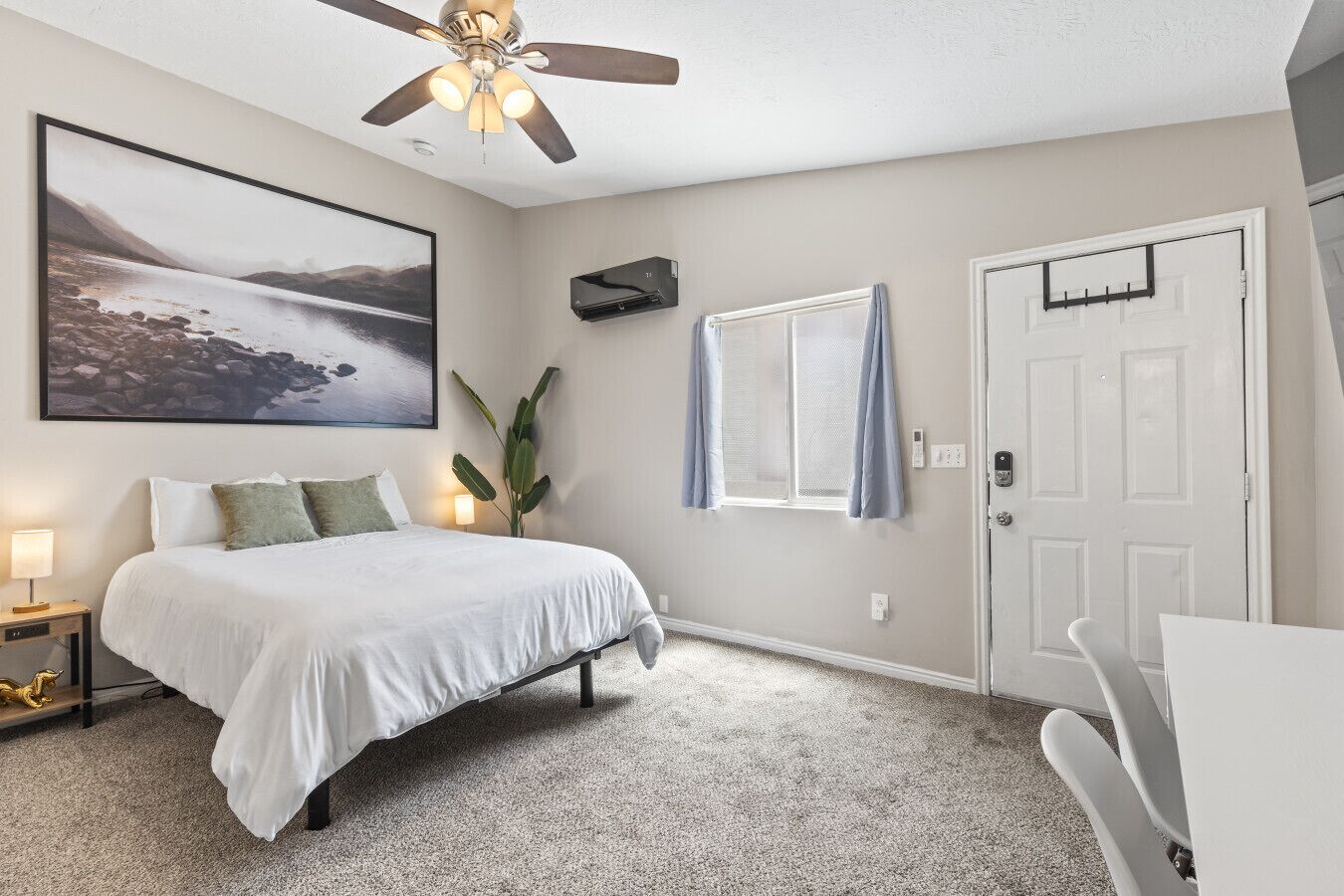 A bedroom with a bed, a ceiling fan, a window with curtains, a door, and a wall-mounted air conditioning unit.