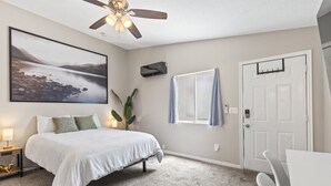 Una camera da letto con un letto, una ventola a soffitto, una finestra con tende, una porta e un condizionatore d'aria a parete.