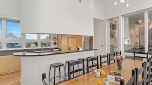 A modern kitchen with a central island, bar stools, and a dining area with a wooden table and chairs. - Matarangi by Avantstay Gulf-front Grayton Beach Retreat Pool + Golf Cart Near Gulf Place (Santa Rosa Beach)