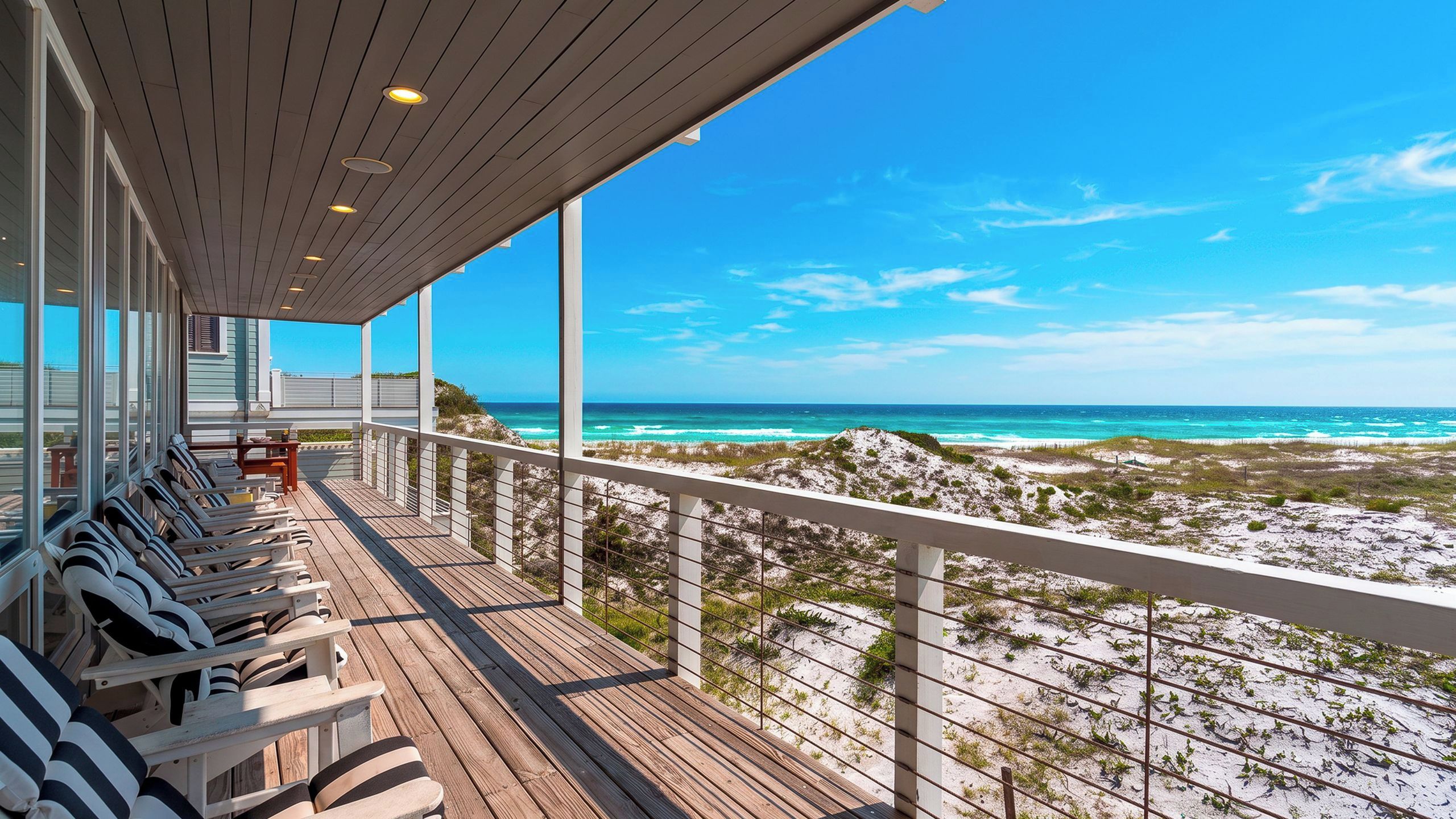 Une terrasse en bois offrant une vue sur la plage, dotée d’une rambarde et de chaises longues.