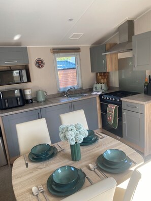 A compact kitchen with a built-in microwave, a stove, and a sink. - Luxury caravan on a 5 star holiday park (Llanrug)