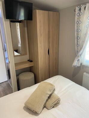 Ein Schlafzimmer mit einem Bett, einem Holzschrank, einem Fernseher und einem Fenster mit Vorhängen.