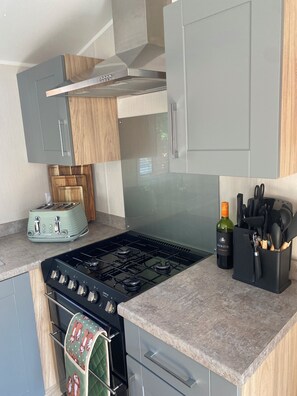 A modern kitchen with a gas stove, a toaster, and a wine bottle. - Luxury caravan on a 5 star holiday park (Llanrug)