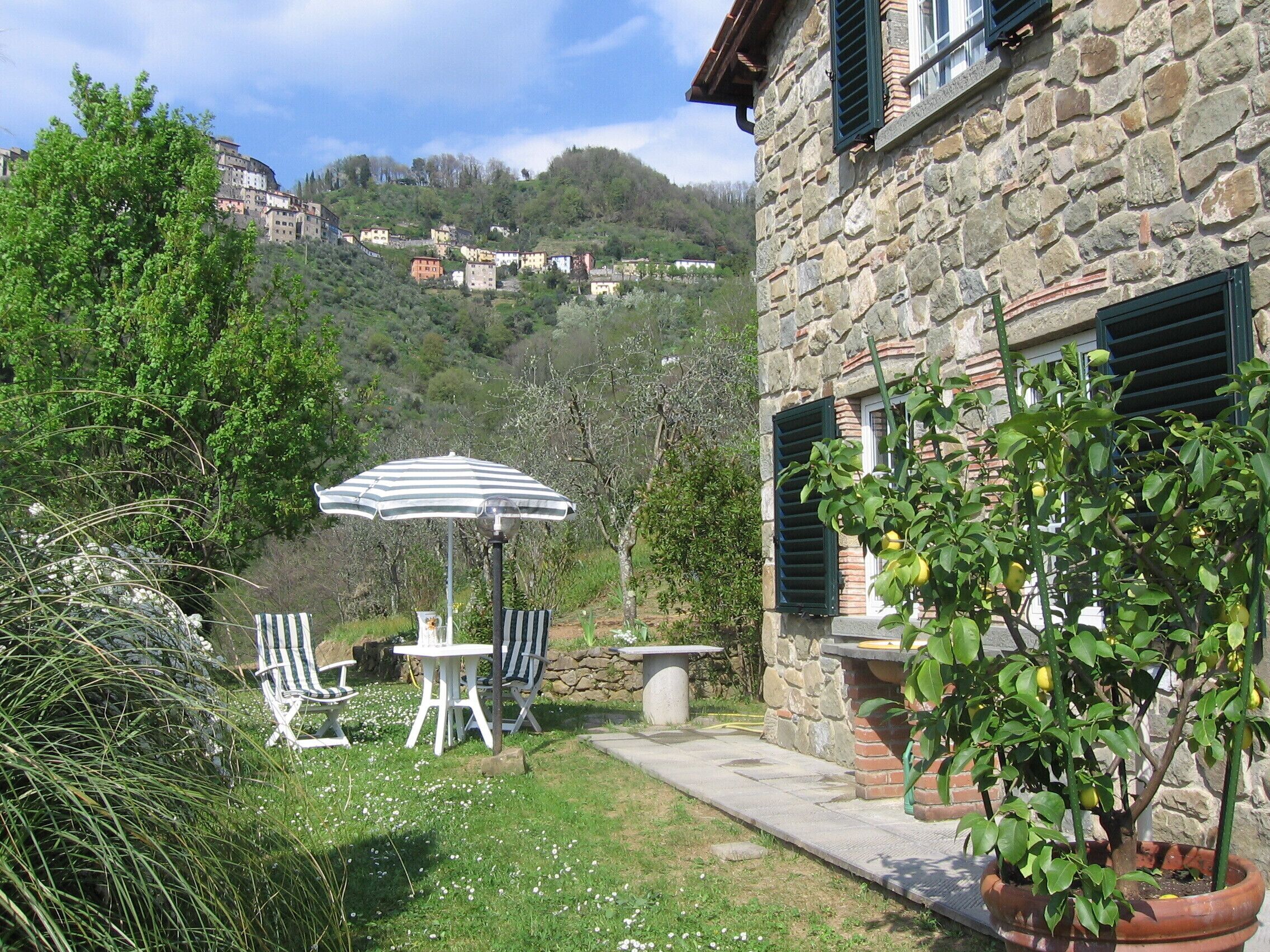 Un bâtiment en pierre doté d’un patio comprenant une table et des chaises, un pot de fleurs et une vue sur une colline parsemée de bâtiments.