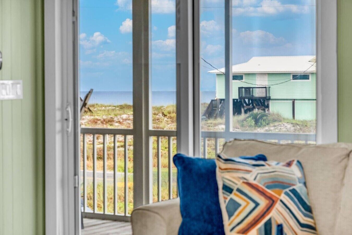 A room with a view of a beach and a house across the water.