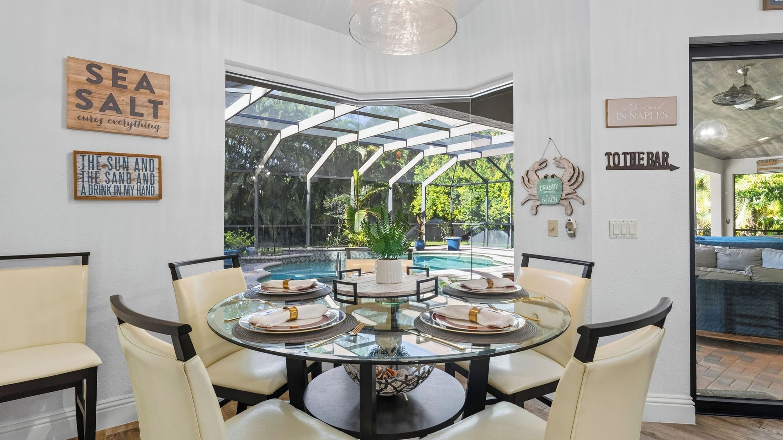 A dining area with a glass table surrounded by chairs, a view of a pool, and various wall decorations.