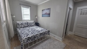Une chambre à coucher avec un lit, une fenêtre avec des stores, un tableau accroché au mur et une porte.