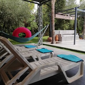 Eine Hängematte zwischen zwei Liegestühlen, im Hintergrund eine Pergola.
