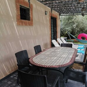 Een terras buiten met een ronde tafel, zwarte wickerstoelen en een hangmat.
