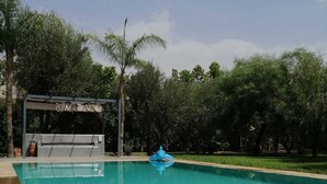 En swimmingpool med en blå uppblåsbar leksak i, omgiven av träd och ett överbyggt område.