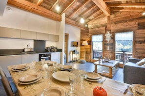 A wooden interior with a dining area set for four, kitchen appliances, and a view through a window. - Wifi, 2nd floor, view resort, fitness, sauna, balcony, parking, ski locker, 82m², Les Gets (Les Gets)