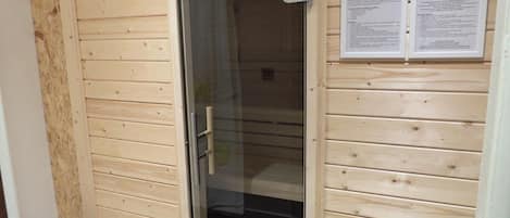 A sauna room with a glass door, wooden walls, and informational posters.