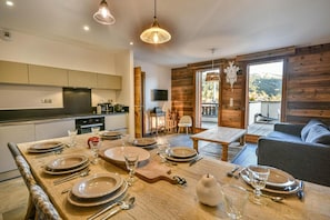 A dining area with a wooden table set for a meal, a sofa, and a view of the outdoors. - Wifi, 1st floor, view resort, fitness, sauna, balcony, parking, ski locker, 82m², Les Gets (Les Gets)