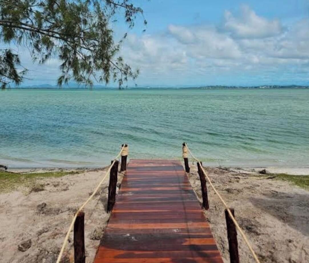 A wooden boardwalk leading to a sandy beach with clear water and a distant shoreline.