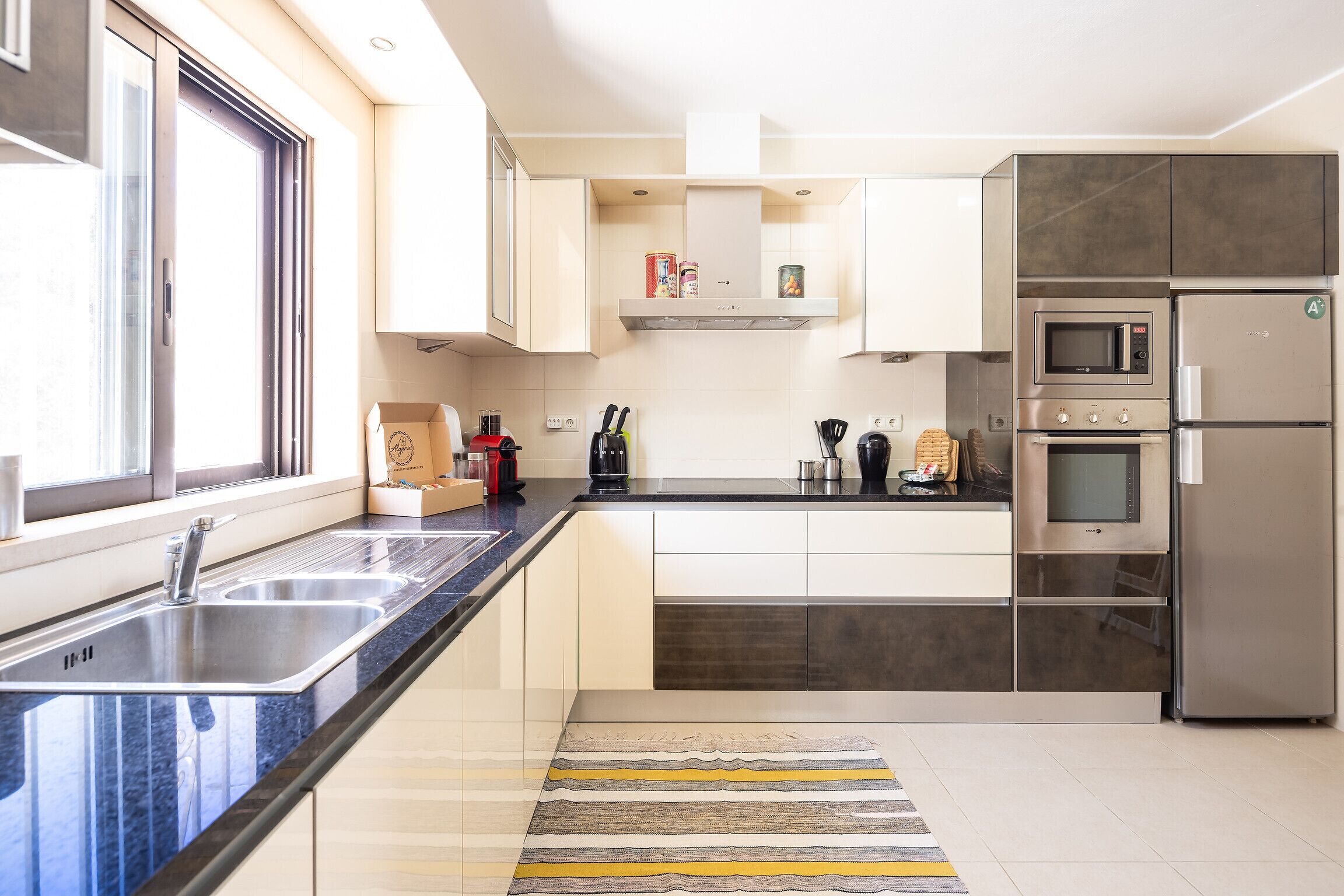 Een moderne keuken met roestvrijstalen apparatuur, een dubbele spoelbak en een raam voor natuurlijk licht.