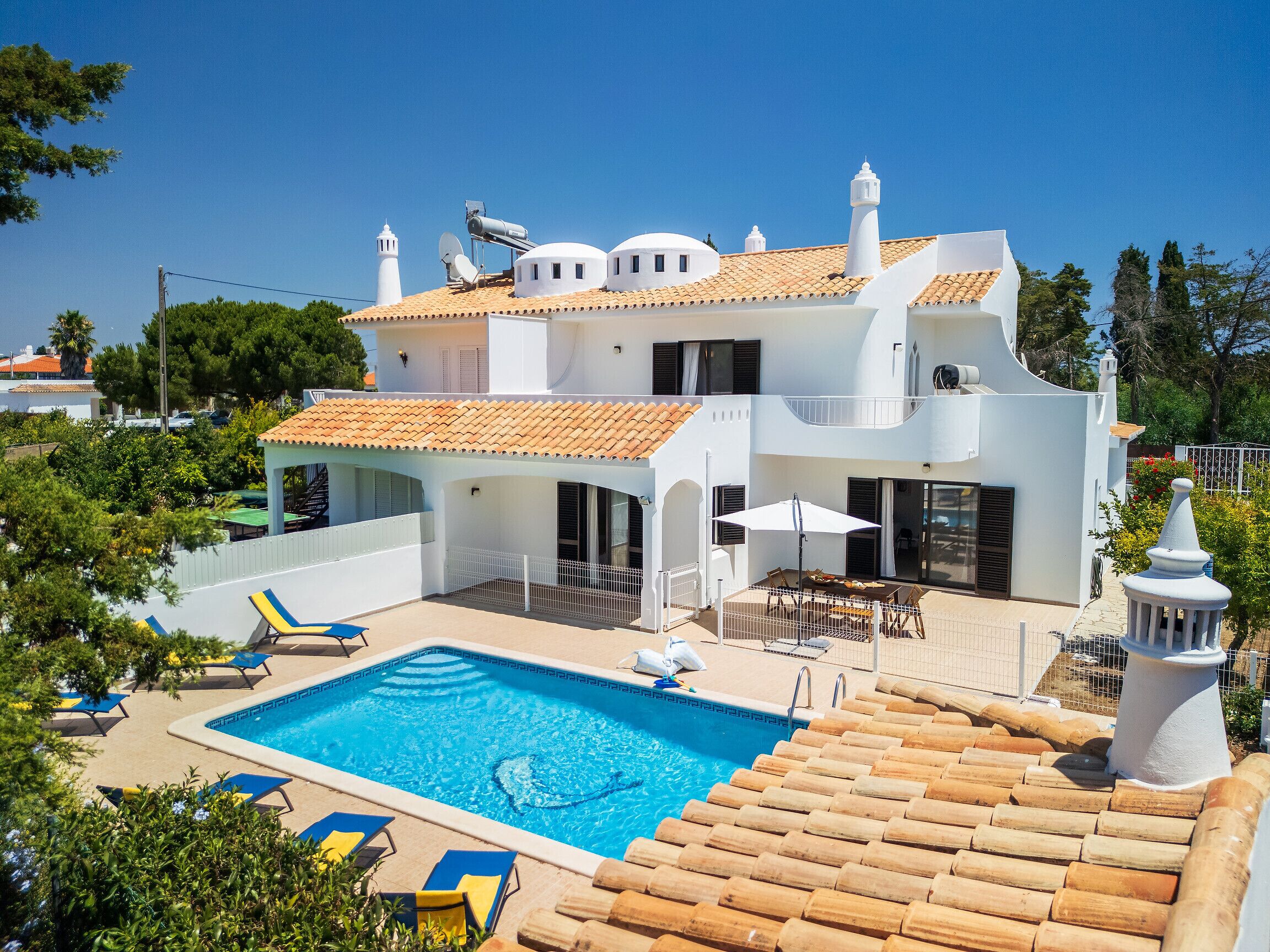 Une maison à deux étages avec une piscine, du mobilier d’extérieur et une clôture blanche.