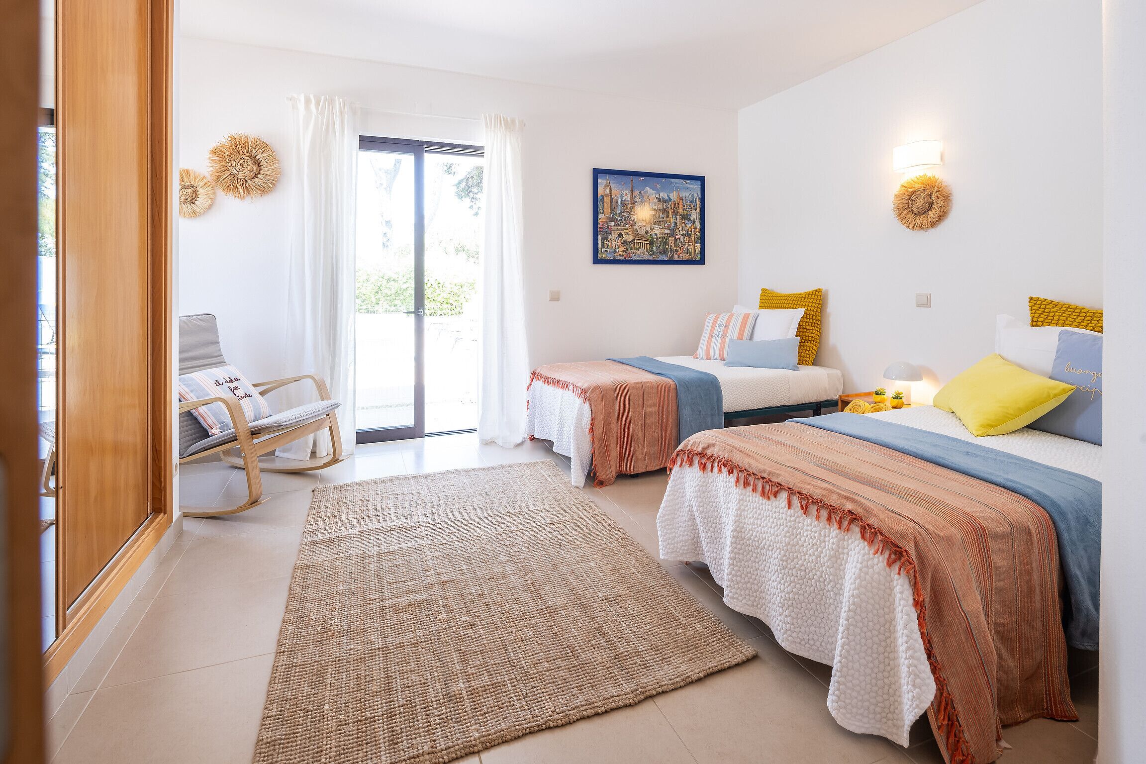 A hotel room with two beds, a sitting area with a chair, a large window, and a painting on the wall.
