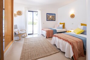 Habitación de hotel con dos camas, una zona de estar con una silla, un ventanal grande y un cuadro en la pared.