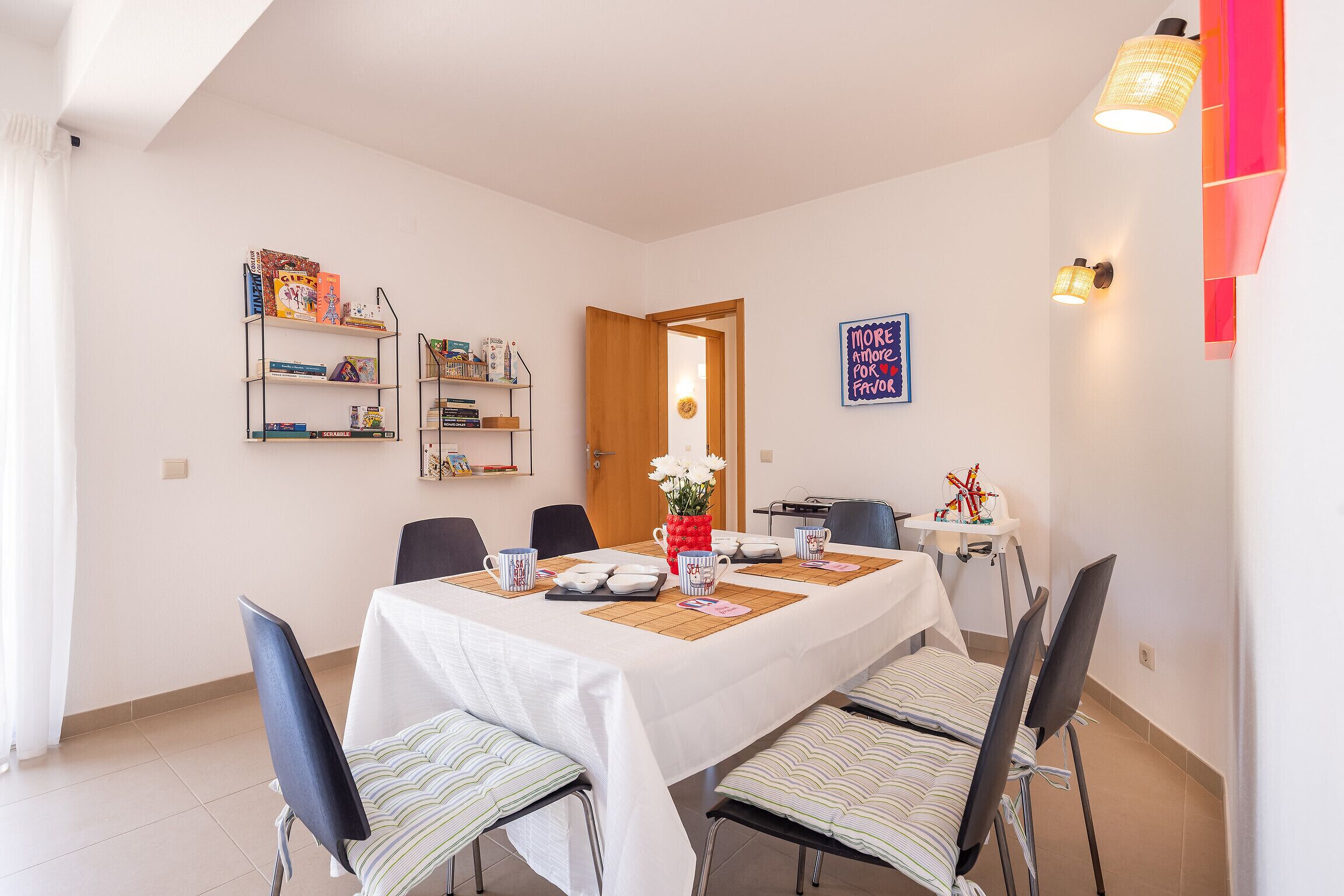 Ein Essbereich mit einem Tisch für vier Personen, Stühlen, einem Bücherregal und einer Wand mit einem dekorativen Element.