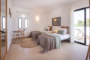 A bedroom with two beds, a desk, and a chair. There is a window with curtains, a painting on the wall, and a view of the outdoors. - CAJI- NEW VILLA NEAR THE BEACH (Albufeira)