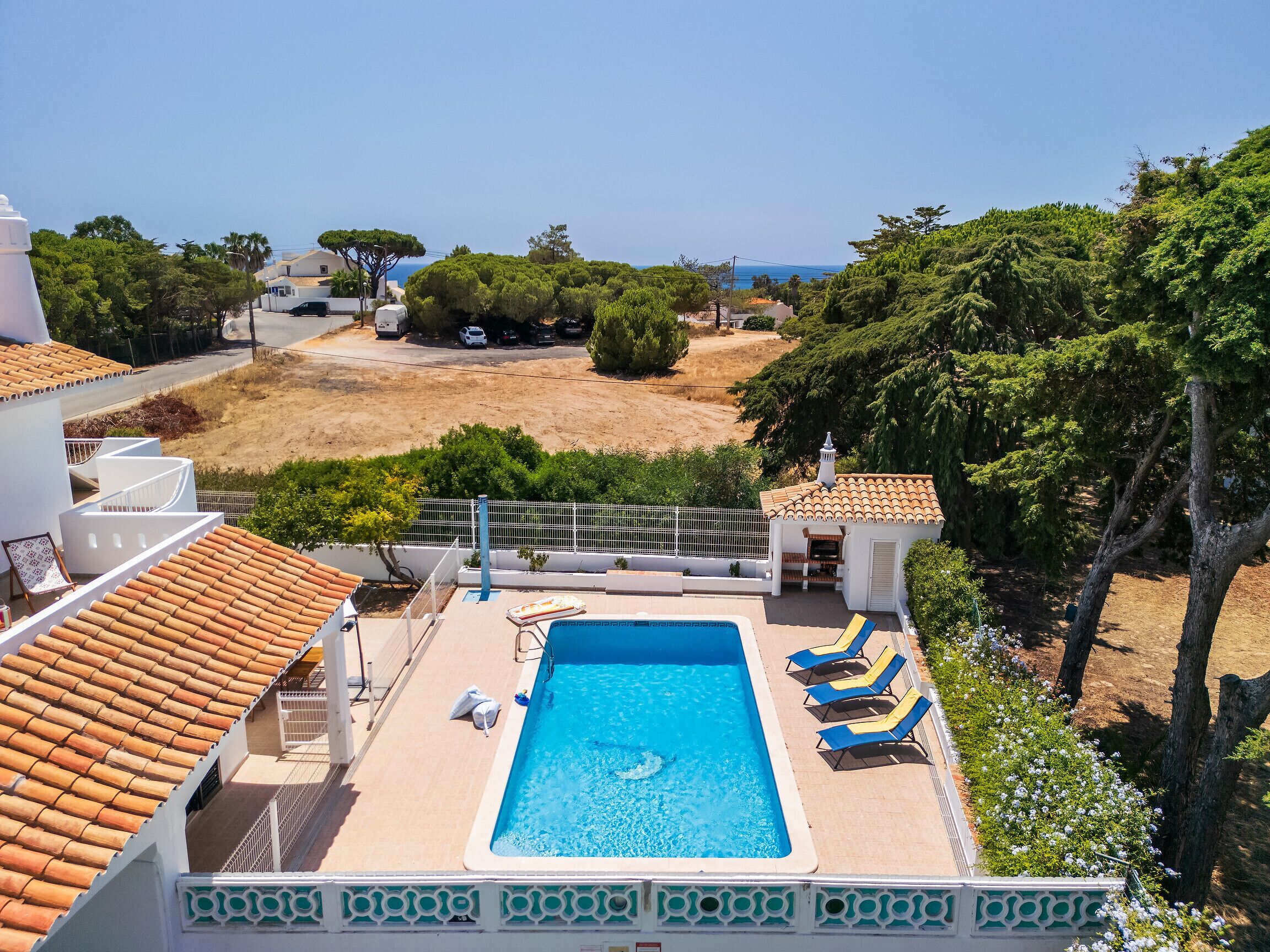 A swimming pool with lounge chairs, a view of the sea, and a white building with a tiled roof.