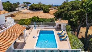 A swimming pool with lounge chairs, a view of the sea, and a white building with a tiled roof. - CAJI- NEW VILLA NEAR THE BEACH (Albufeira)