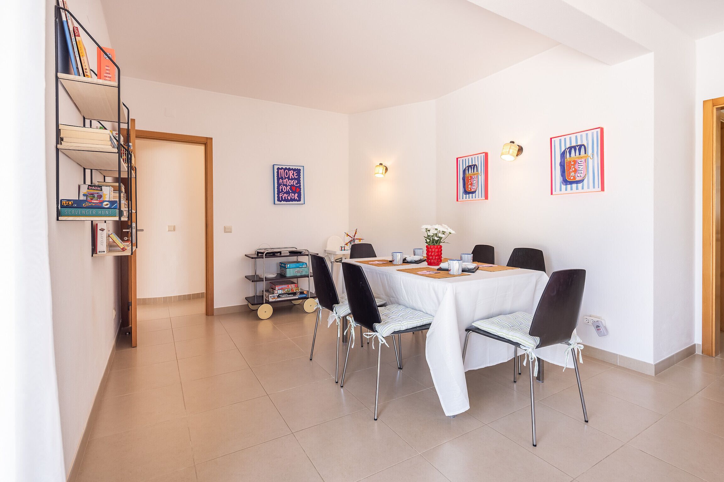 Comedor con una mesa dispuesta para cuatro personas, rodeada de sillas, en una habitación con piso de baldosas y paredes blancas.