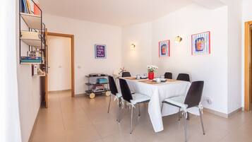 Comedor con una mesa dispuesta para cuatro personas, rodeada de sillas, en una habitación con piso de baldosas y paredes blancas.