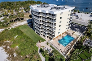 A multi-story hotel with a rooftop pool, surrounded by greenery and a beach. - Gulffront Paradise at Vacation Villa (Fort Myers Beach)