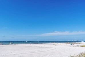 A beach with a clear sky, calm sea, and a few boats. - Gulffront Paradise at Vacation Villa (Fort Myers Beach)