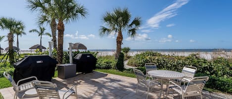 Eine Terrasse im Freien mit Blick auf den Strand, inklusive Grill, Sitzbereich und Sonnenschirmen.